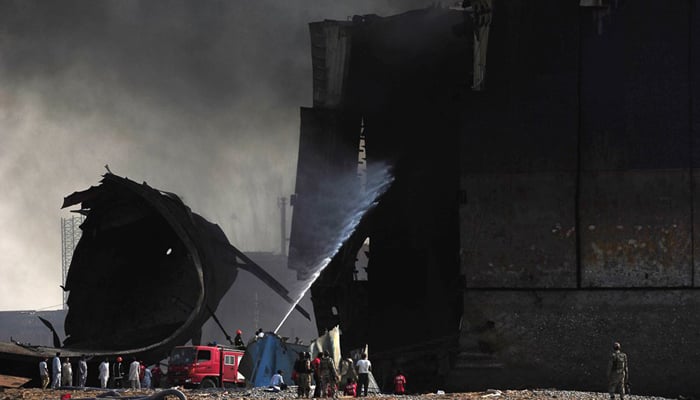 Labourers look on as the fire fighters attempt to put out the fire. PHOTO: AFP