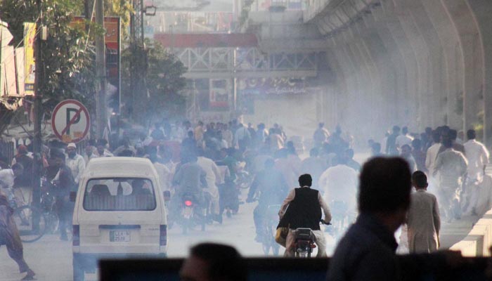 People run as policemen release tear gas to disperse supporters of Awami Muslim League at Committee Chowk.