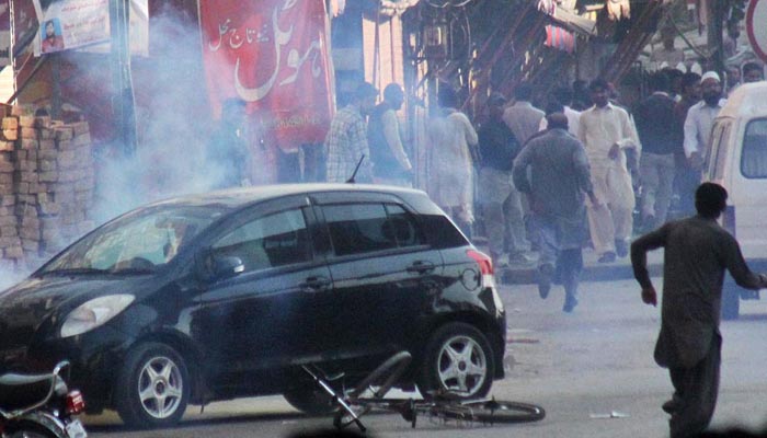 People run as policemen release tear gas to disperse supporters of Awami Muslim League at Committee Chowk