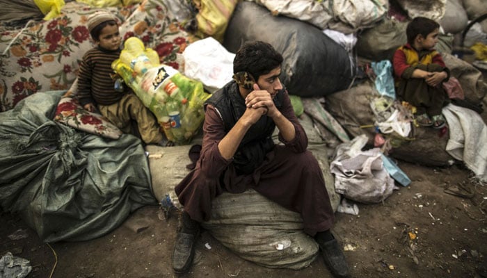 Afghan refugees sit on sacks filled with used plastic items to sell at their makeshift shelter in a slum on the outskirt of Lahore January 12, 2015.—Photo by Reuters