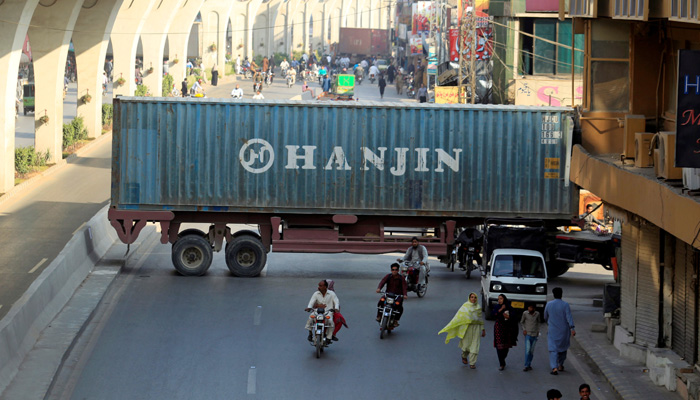 Motorcyclists pass through a gap in a barricade set up using shipping containers near the venue of a planned protest gathering organised by Awami Muslim League