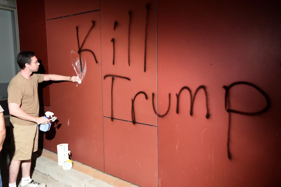 A man tries to remove "Kill Trump" graffiti as demonstrators riot in Oakland.