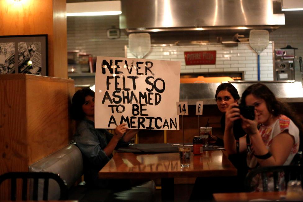 Patrons hold a sign as people march by while protesting the election of Trump in downtown Los Angeles. 