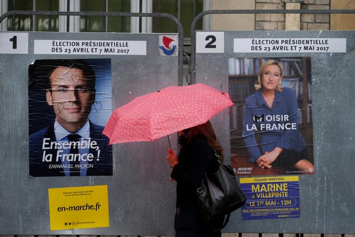null A woman walks past the new official posters for the candidates for the 2017 French presidential election, Emmanuel Macron, head of the political movement En Marche !, or Onwards !, (L) and Marine Le Pen, French National Front (FN) political party leader (R), in Paris, France, April 28, 2017. REUTERS