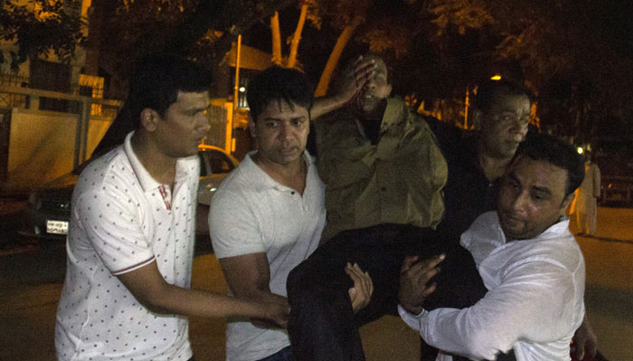 People carry an injured man near the Holey Artisan Bakery restaurant during an attack by unidentified gunmen