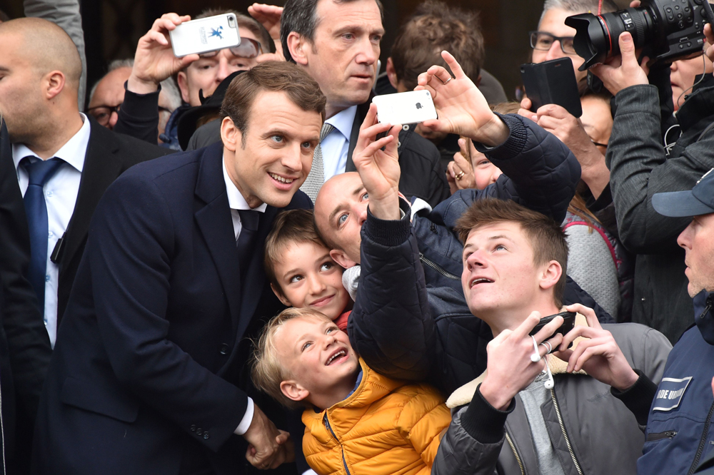 French presidential election candidate for the En   Marche ! movement Emmanuel Macron (L) poses for a   ´selfie´ with supporters after voting in Le   Touquet, northern France, on May 7, 2017, during   the second round of the French presidential   election. / AFP / Philippe HUGUEN