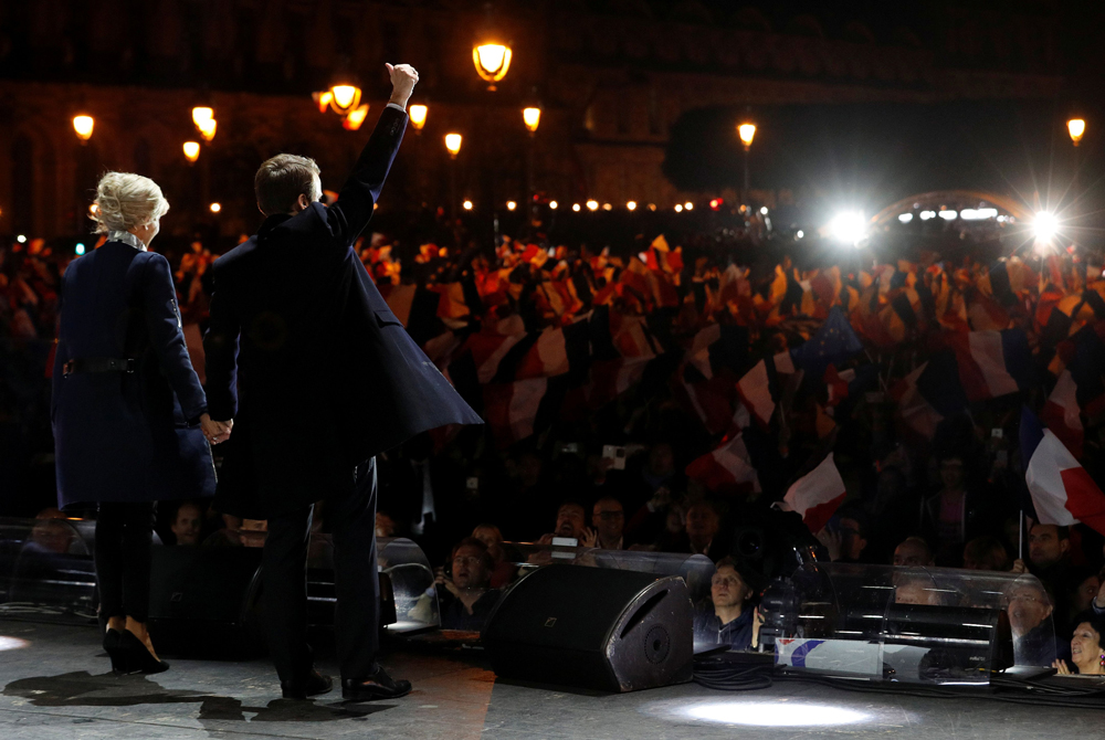 French president-elect Emmanuel Macron (C) holds   his wife, Brigitte Trogneux (L) by the hand as he   gestures on stage after delivering a speech in   front of the Pyramid at the Louvre Museum in   Paris on May 7, 2017, after the second round of   the French presidential election. AFP / POOL /   Philippe Wojazer