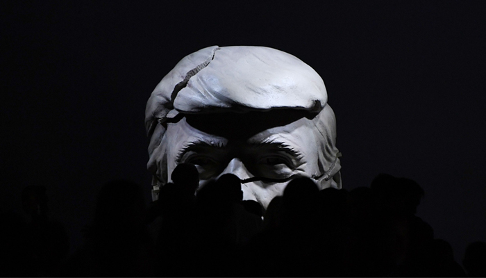 A cracked bust representing US president Donald Trump is visible behind people walking on a catwalk during the Madrid Fashion Week, Madrid, September 16, 2017. AFP/Gabriel Bouys