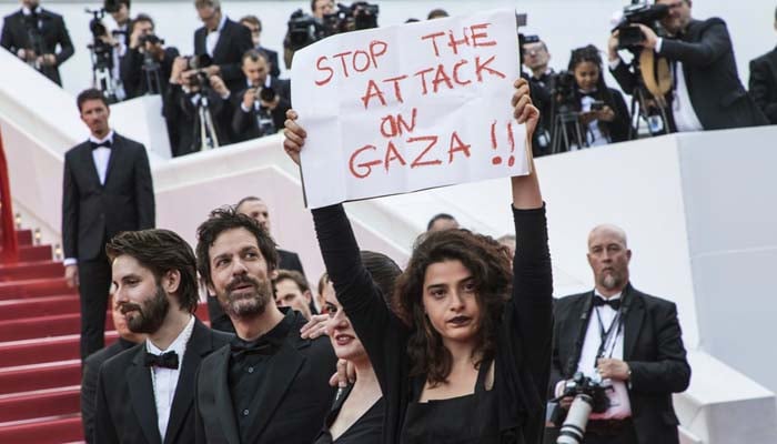 Lebanese actor holds sign reading 'Stop the attack on Gaza' as she walks Cannes red carpet