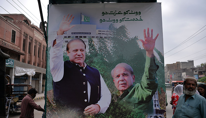 Supporters of former prime minister Nawaz Sharif stand beside a poster featuring Nawaz Sharif (L) and his younger brother Shehbaz Sharif at the venue where Shahbaz will lead a rally towards the airport ahead of the arrival of Nawaz from London, in Lahore on July 13, 2018. Photo: AFP 