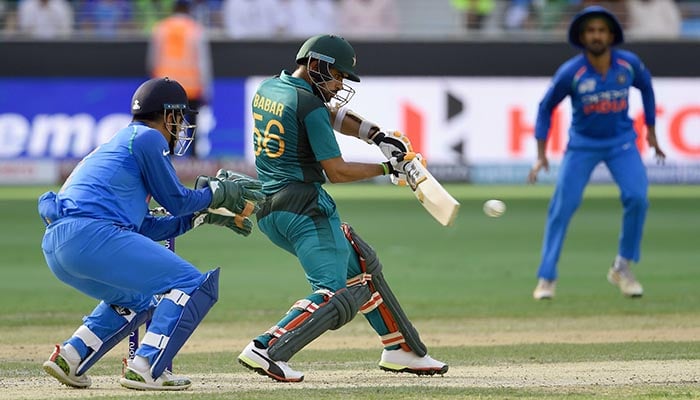 Pakistan batsman Babar Azam plays a shot as as Indian wicketkeeper Mahendra Singh Dhoni (L) looks on during the one day international (ODI) Asia Cup cricket match between Pakistan and India at the Dubai International Cricket Stadium in Dubai on September 19, 2018 - AFP