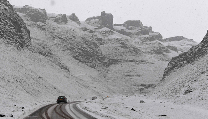 A car is driven on a snow-covered road as it passes through Winnats Pass near Castleton England