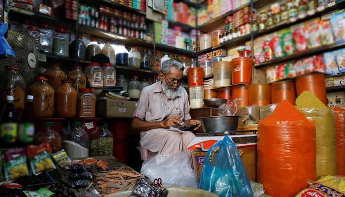 A shopkeeper uses a calculator while selling spices and grocery items along a shop in Karachi, Pakistan June 11, 2021. -REUTERS