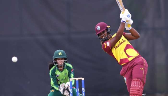 A West Indian bastman playing a shot while Pakistani wicketkeeper looks on.