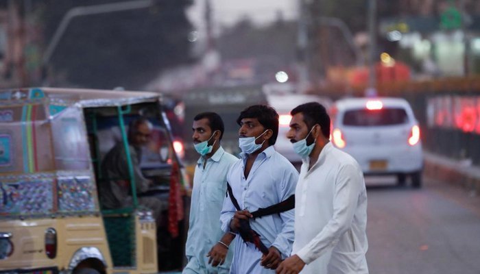 Men wearing face masks on their chins cross a street in Karachi as Pakistan eases coronavirus restrictions amid a sharp drop in infections. Photo: Reuters