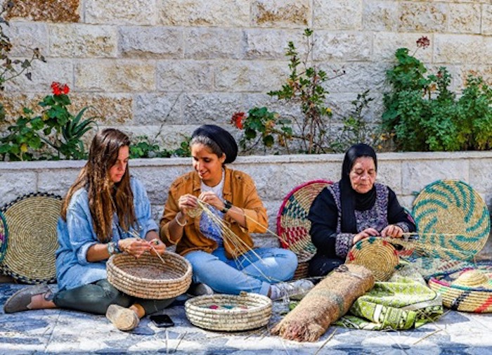 During their trip to Kifl Haris in Salfit, Umm Samer teaches travel bloggers Malak Hassan and Bisan Alhajhasan how to make trays woven from wheat straw.  Photo: Courtesy of Ahlan Palestine