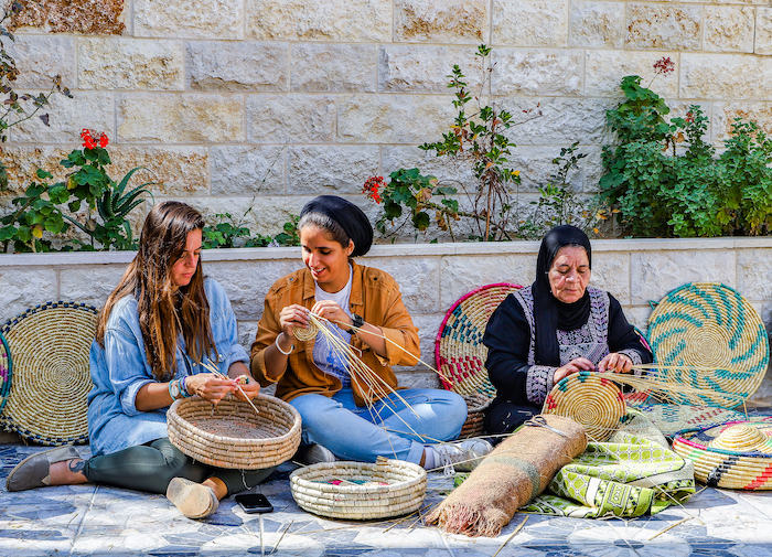 During their trip to Kifl Haris in Salfit, Umm Samer teaches travel bloggers Malak Hassan and Bisan Alhajhasan how to make trays weaved of wheat straws. Photo: Courtesy Ahlan Palestine