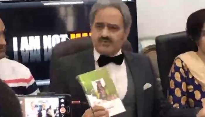 Clad in a tuxedo, Kashif Mirza speaks at a news conference in Lahore, clutching the book I am not Malala in his hand.