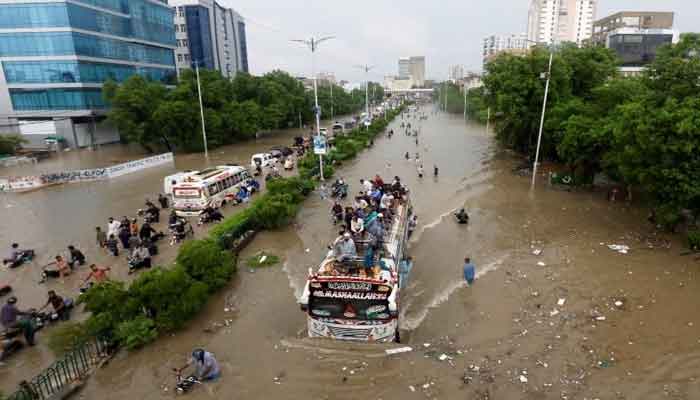 People sit atop a bus roof while others wade through a flooded road during monsoon rain in Karachi on August 27, 2020. — Reuters