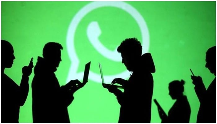 Silhouettes of mobile phone and laptop users are seen next to a screen projection of the WhatsApp logo, March 18, 2018. — Reuters/File