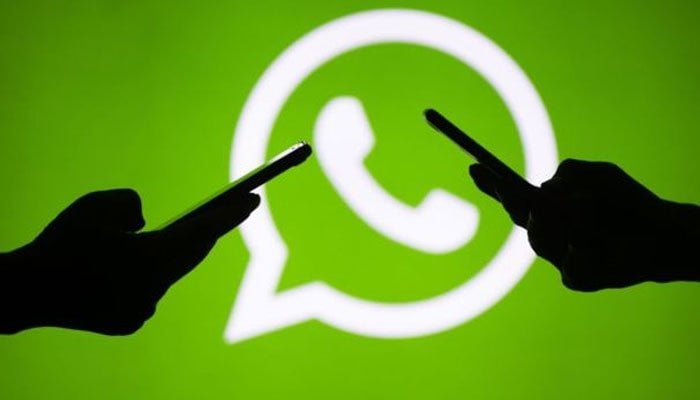 Silhouettes of mobile phone and laptop users are seen next to a screen projection of the WhatsApp logo, March 18, 2018. — Reuters/File