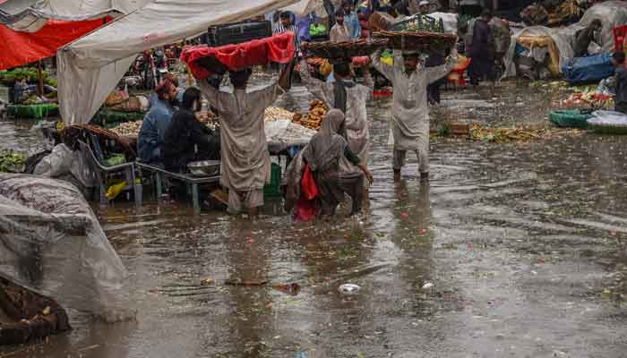 Vendors carry wares on their heads to shelter from the rains amid a waterlogged street along a market area during heavy monsoon rains in Lahore on July 20, 2021. — AFP/Arif Ali