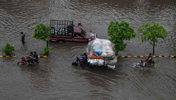 Commuters make their way through a flooded street after heavy monsoon rains in Lahore on July 20, 2021. — AFP/Arif Ali