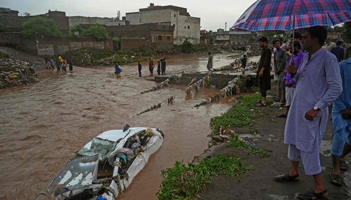 Residents gather as they look at a damaged car submerged in the flood waters after heavy monsoon rains in Islamabad on July 28, 2021. — AFP