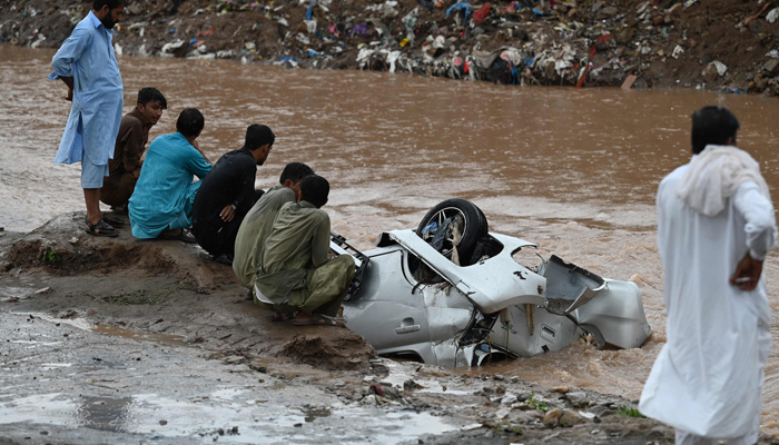 Residents gather as they look at a damaged car submerged in flood waters after heavy monsoon rains in Islamabad on July 28, 2021. — AFP