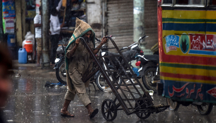 A labourer covers himself as he pushes a cart on a street under the rain in Karachi on August 6, 2020. — AFP/Asif Hassan