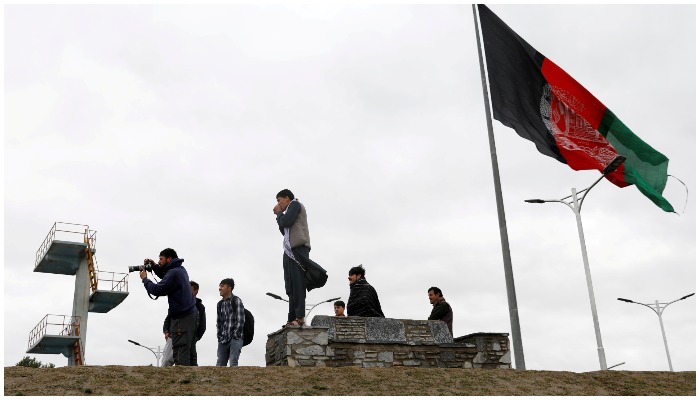 Youths take pictures next to an Afghan flag on a hilltop overlooking Kabul, Afghanistan, April 15, 2021. REUTERS/Mohammad Ismail/File Photo.