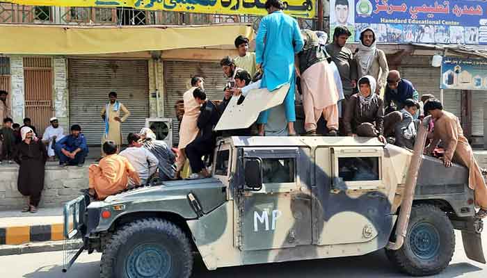 Taliban fighters and local residents sit over an Afghan National Army (ANA) humvee vehicle along the roadside in Laghman province on August 15, 2021. — Photo by AFP