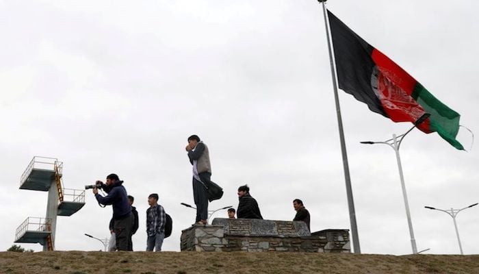 Youths take pictures next to an Afghan flag on a hilltop overlooking Kabul, Afghanistan, April 15, 2021. Photo: Reuters