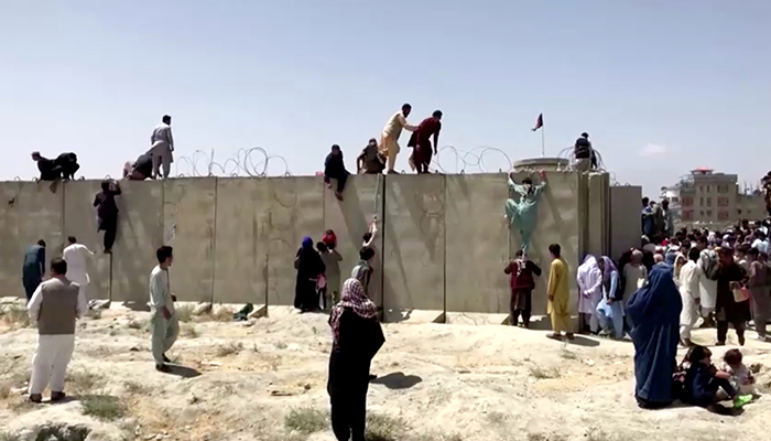 People climb a barbed wire wall to enter the airport in Kabul, Afghanistan August 16, 2021, in this still image taken from a video. — Reuters