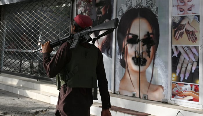 A Taliban fighter walks past a beauty saloon with images of women defaced using a spray paint in Shar-e-Naw in Kabul on August 18, 2021. — AFP/File