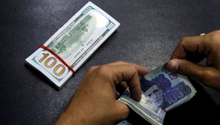 A trader counts Pakistani rupees beside a stack of US dollars. Photo: File