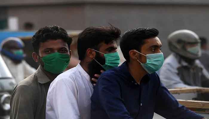 Three men on board a motorcycle are seen wearing surgical masks in this AFP file photo from Pakistan.