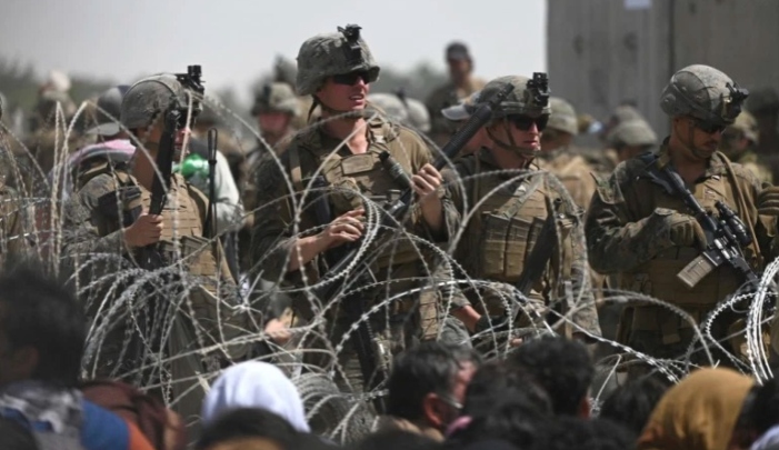 US soldiers stand guard as Afghans sit on a roadside near the military part of the airport in Kabul [Wakil Kohsar/AFP]