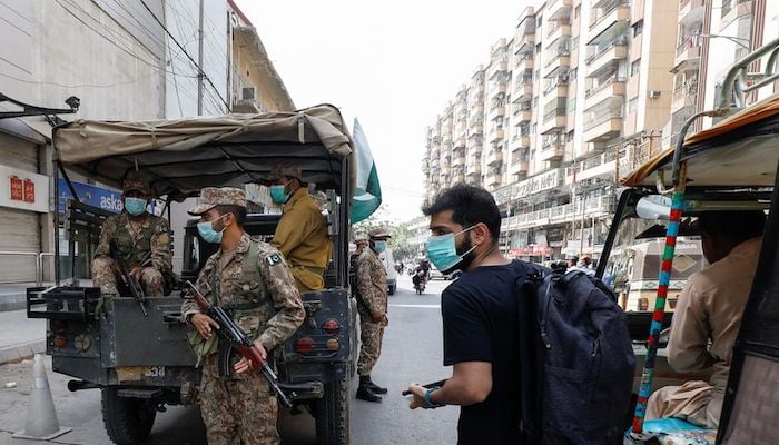 A resident wearing a protective mask walks past Pakistan Army soldiers on patrol to enforce coronavirus disease (COVID-19) safety protocols in Karachi, Pakistan April 28, 2021. Photo: Reuters