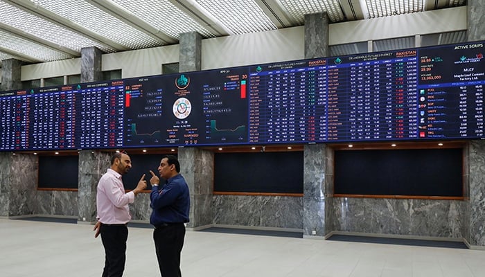 Men are seen talking in front of electronic board displaying share market prices during a trading session at the Pakistan Stock Exchange (PSX) in Karachi. — Reuters