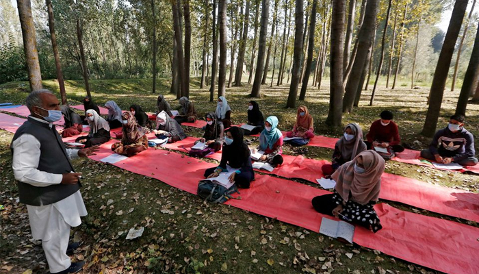 Students wearing masks attend their class under the trees as they maintain social distancing outside their school, amid the coronavirus disease. — Reuters