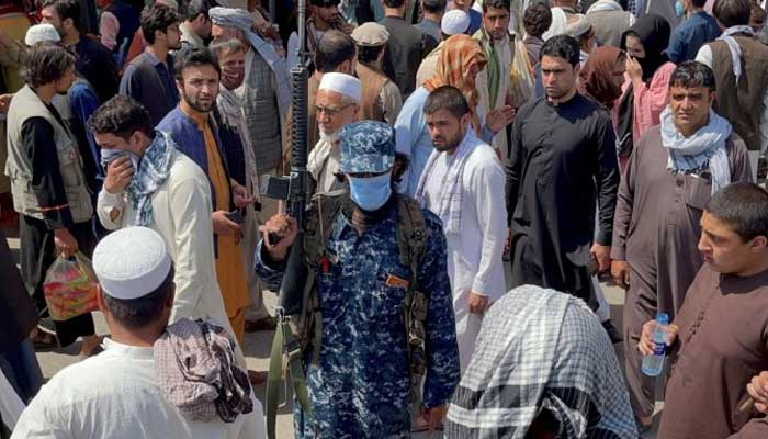 Member of Taliban security forces stands guard among crowds of people in a street in Kabul. — Reuters