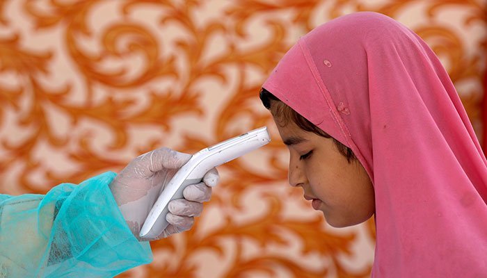 A health worker wearing protective gear checks a girls temperature, at a walk-through screening and testing facility for coronavirus disease (COVID-19) in Karachi, Pakistan. Photo: Reuters