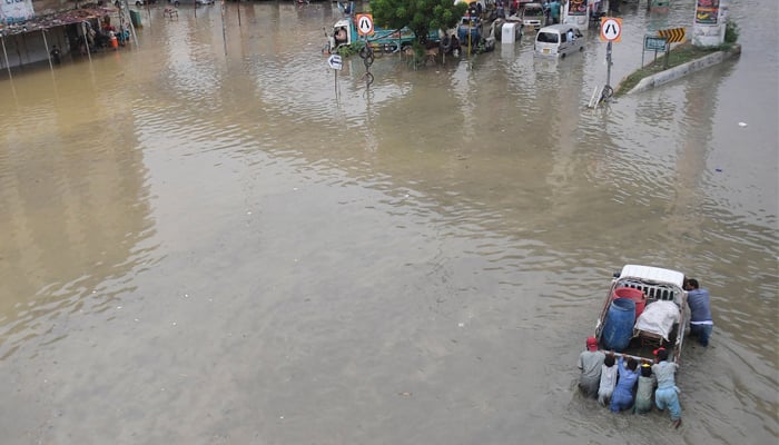 Men push a vehicle through a flooded street after a heavy rainfall in Karachi on September 23, 2021. — AFP