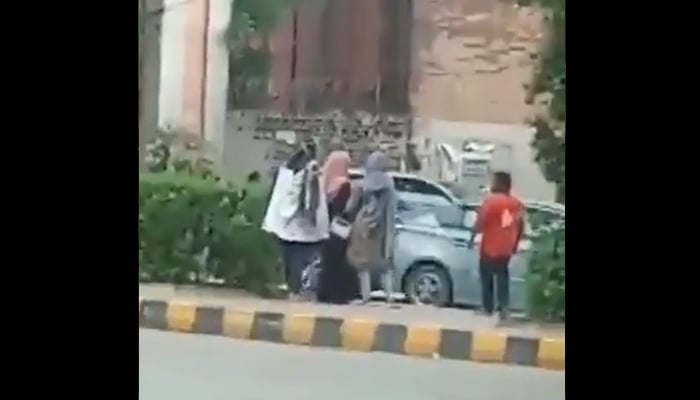 Three women stand near a bus stop as a man tries to interact with them. Photo: Twitter screengrab