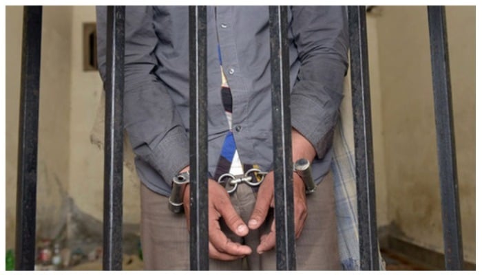A man wearing handcuffs standing behind the bars. Photo: AFP.
