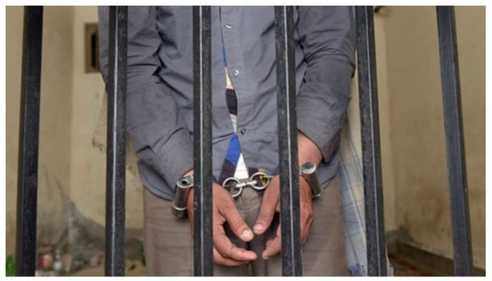 A man wearing handcuffs standing behind the bars. Photo: AFP.