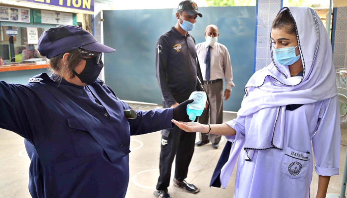Staff sanitises the hands of students at the entrance of Hayat Girls School in Hyderabad, on August 30, 2021. — APP/File