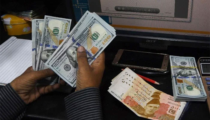 A currency dealer is counting dollar notes while Rs5,000 notes are placed on the desk. — AFP/File