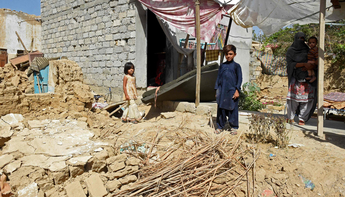 A woman and her children stand beside their collapsed mud house following an earthquake in the remote mountainous district of Harnai on October 7, 2021, as at least 20 people were killed and dozens injured when a shallow earthquake hit southwestern Pakistan in the early hours of October 7. — AFP